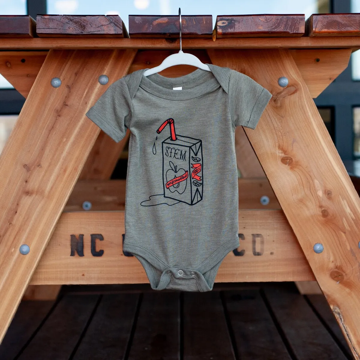 Gray Stem Ciders baby onesie hanging from a picnic table