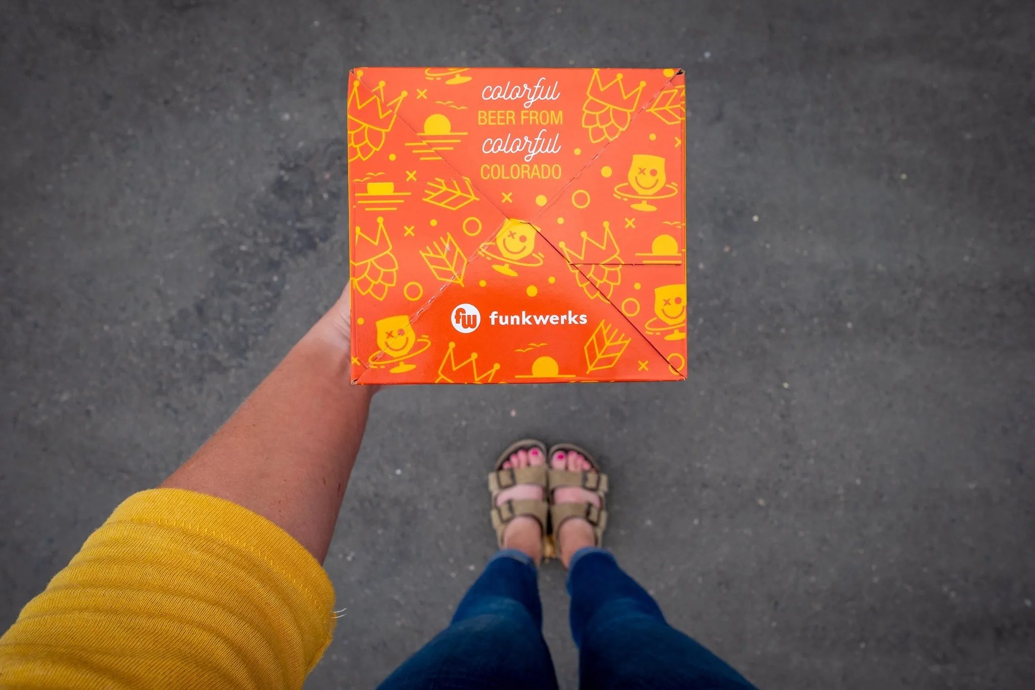 Looking down at an orange Funkwerks to-go box held at a person's feet
