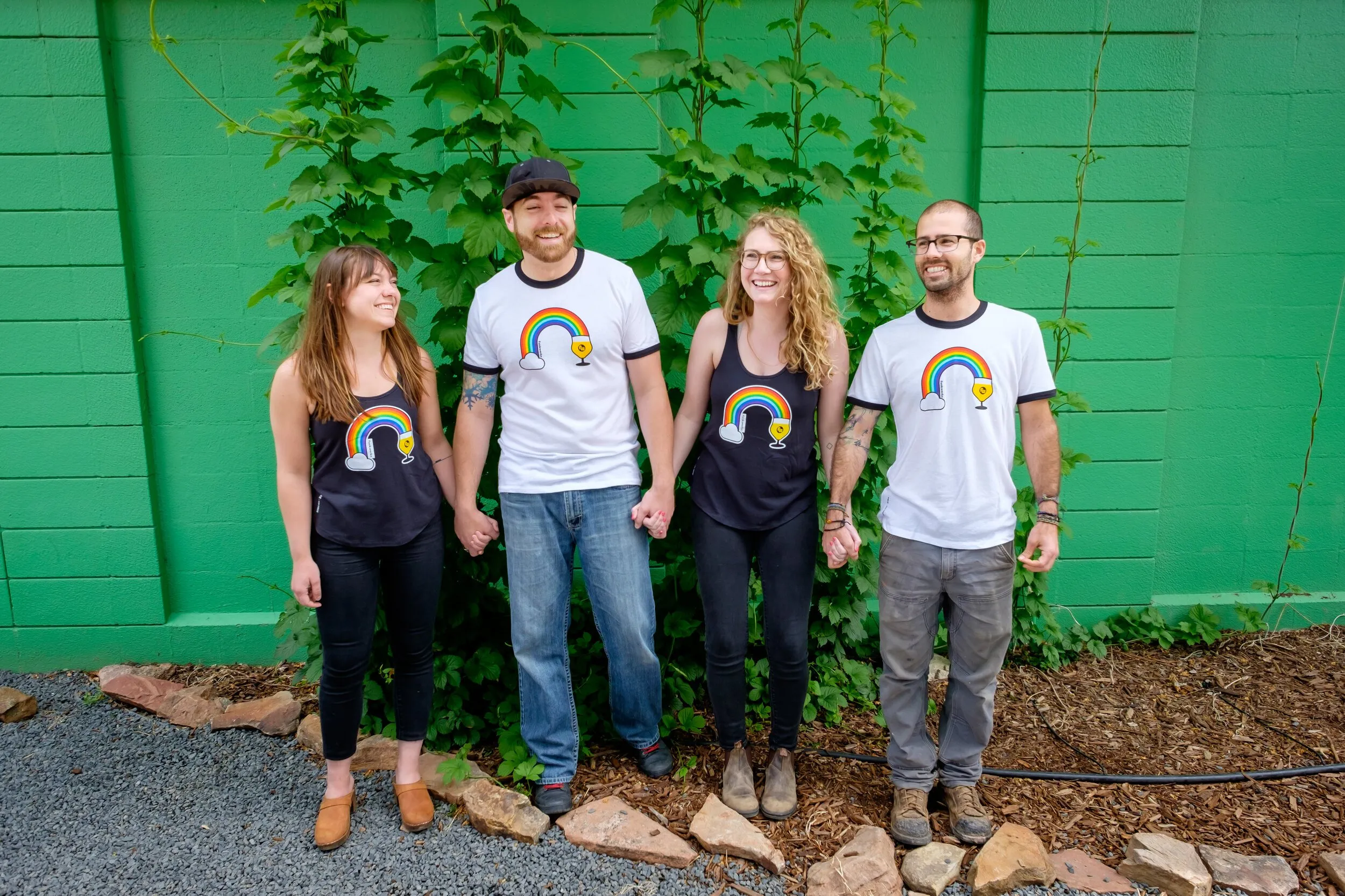 Four people in Funkwerks Pride tees and tanks in front of a green wall
