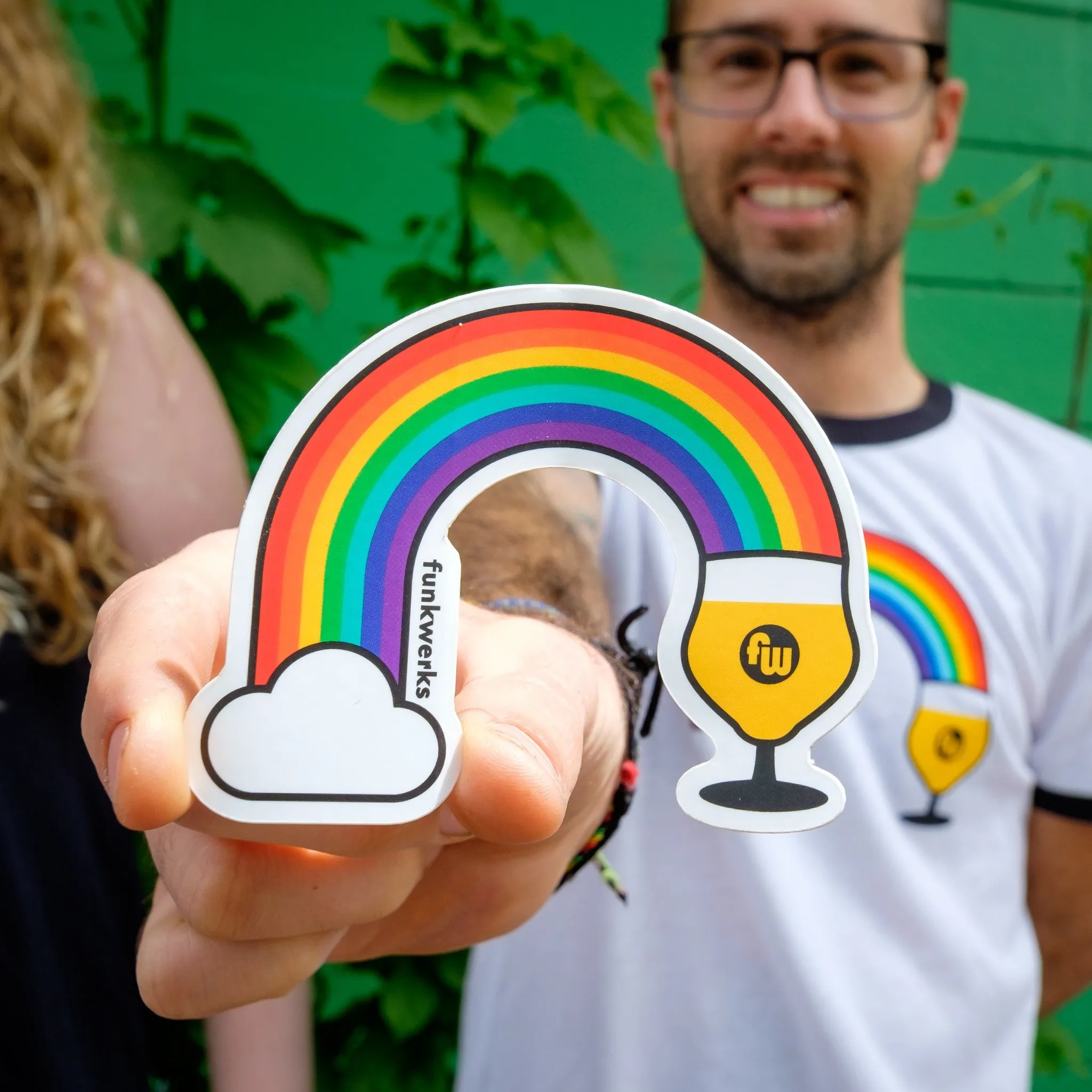 Hand holding a rainbow Funkwerks sticker over a Pride tee