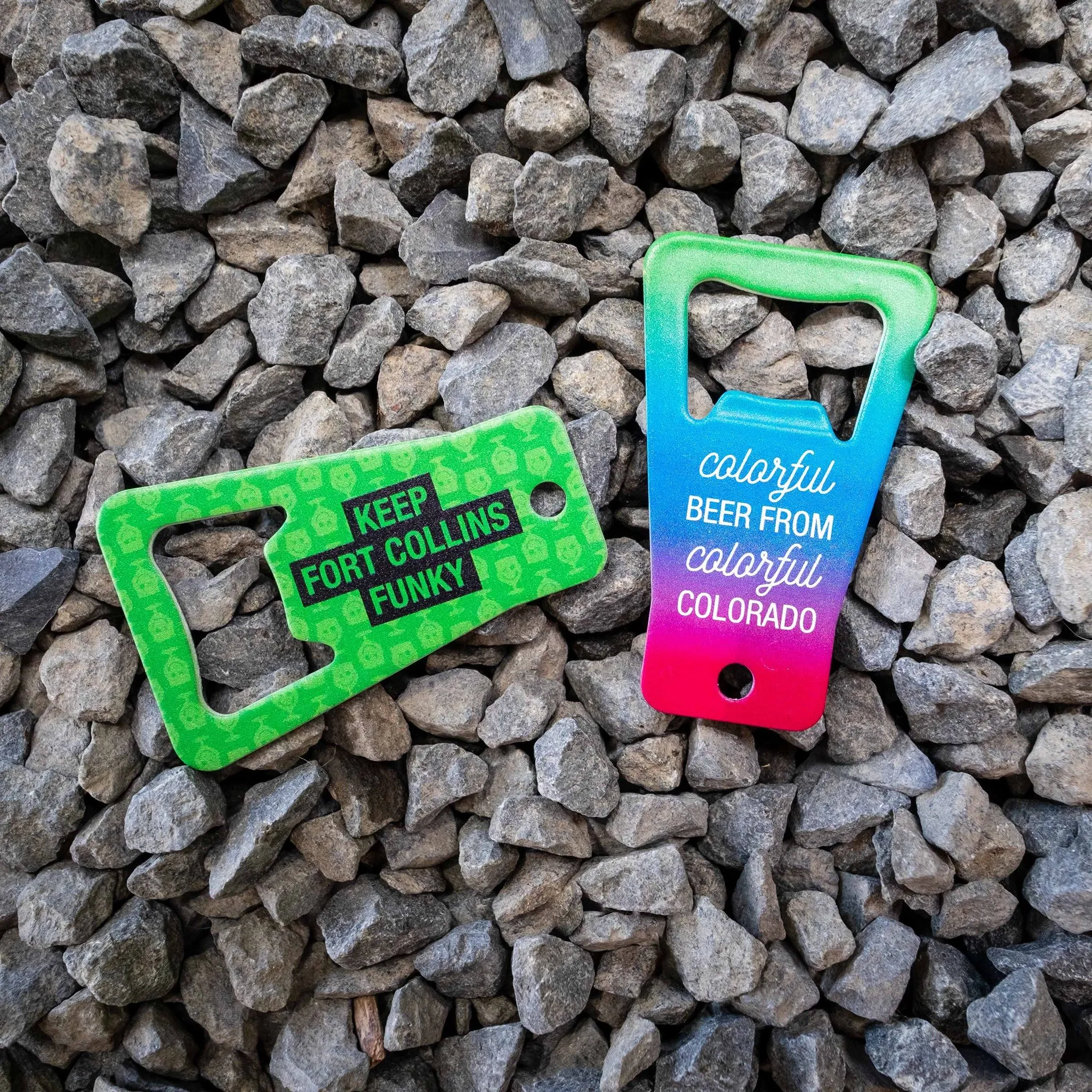 Green and teal Funkwerks bottle opener keychains on gravel