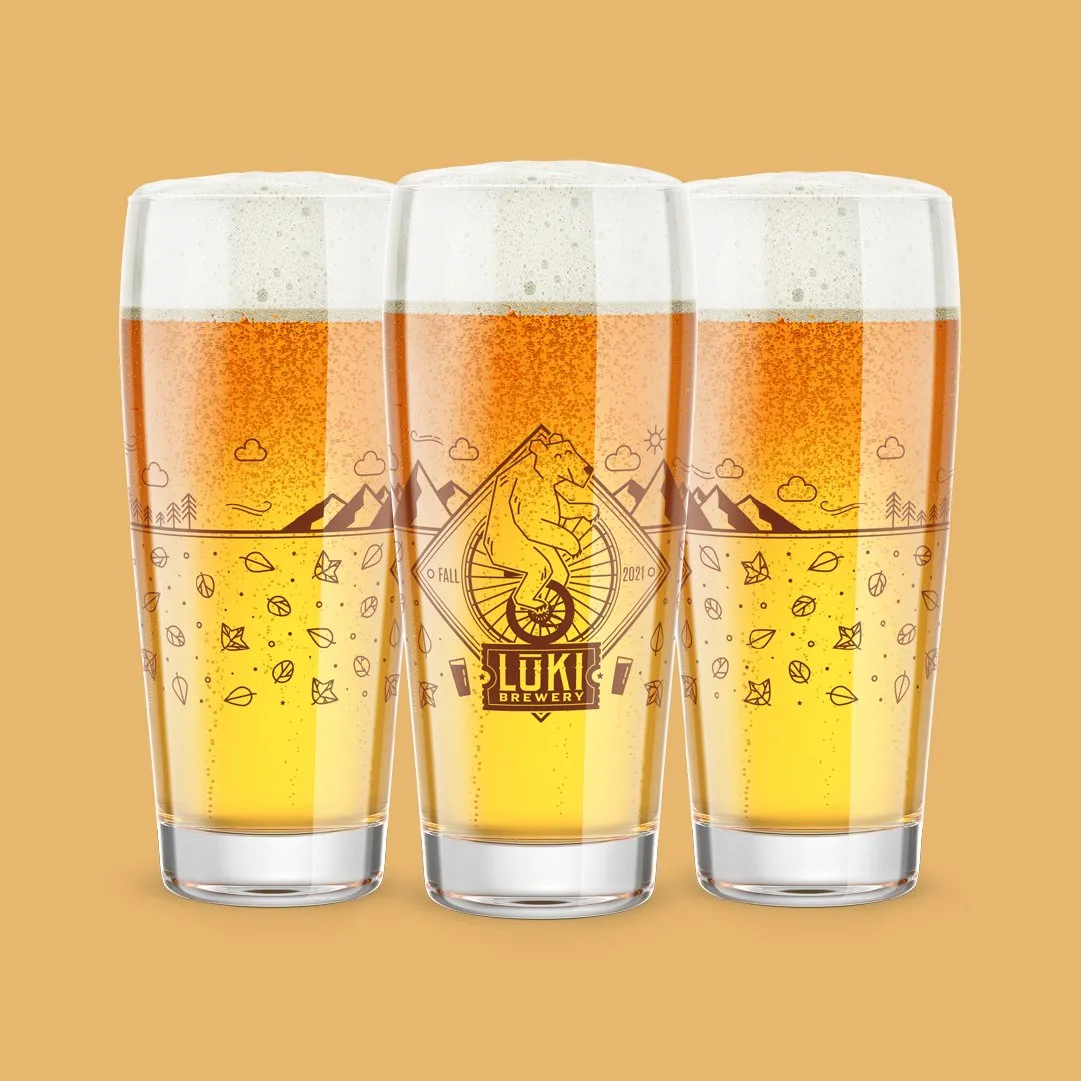 Three Loki pint glasses illustrated with a mountain campfire scene, on mustard